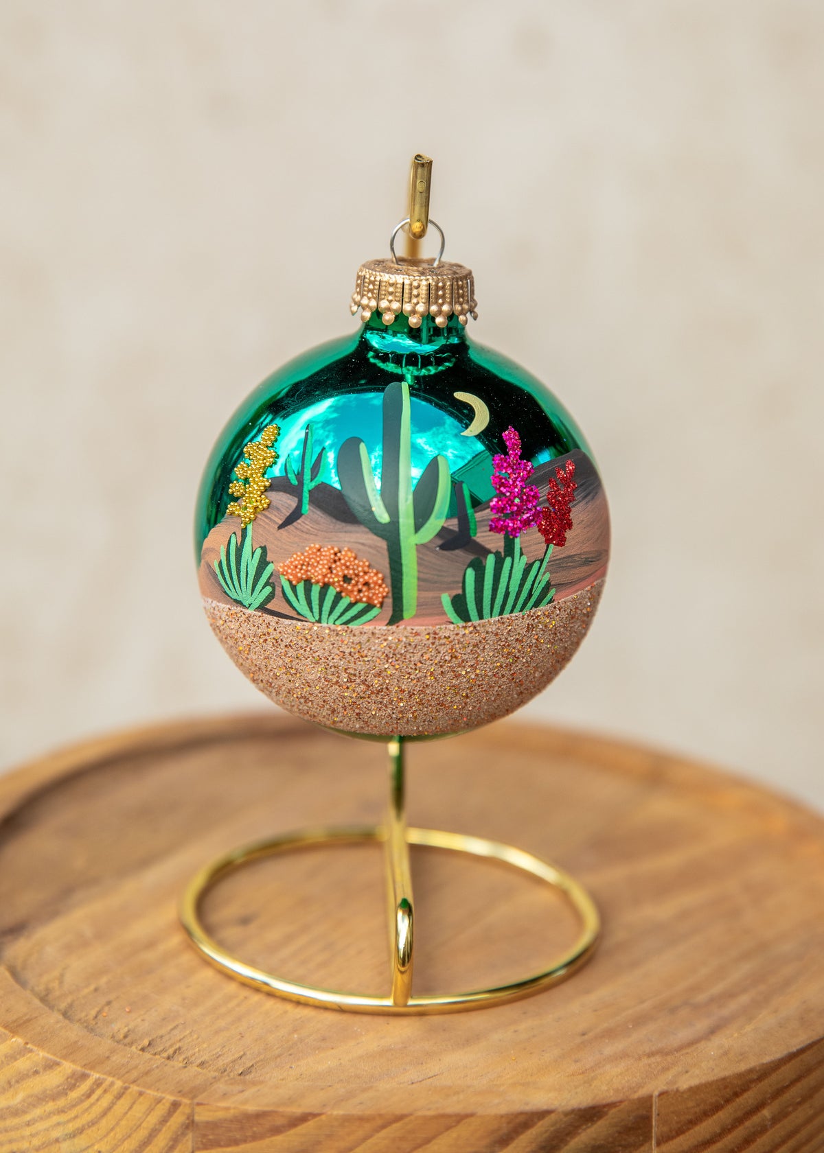 Desert Moonlight Hand Painted glass ornament by Brenda, a saguaro and blooming cactus under a crescent moon on a teal ornament