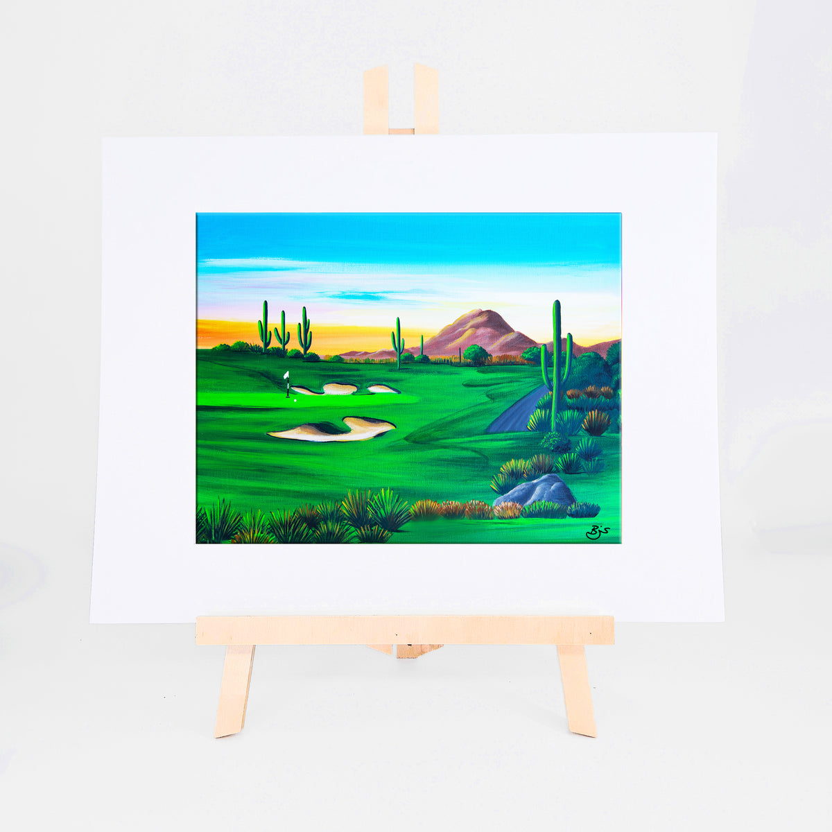 Desert Golf, Brenda's painting of a green desert golf course among sand bunkers, saguaros, and mountains at sunrise, shown as a matted 8x10 art print