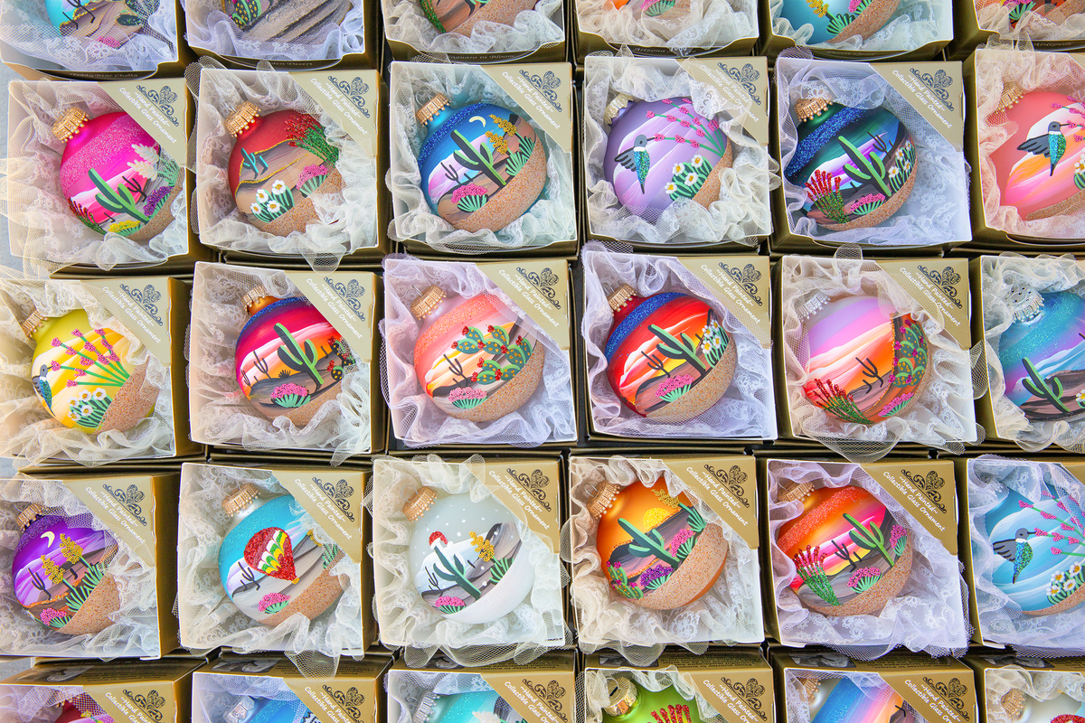 Overhead view of about 30 assorted Hand Painted ornaments arranged in a grid, each in its gold gift box