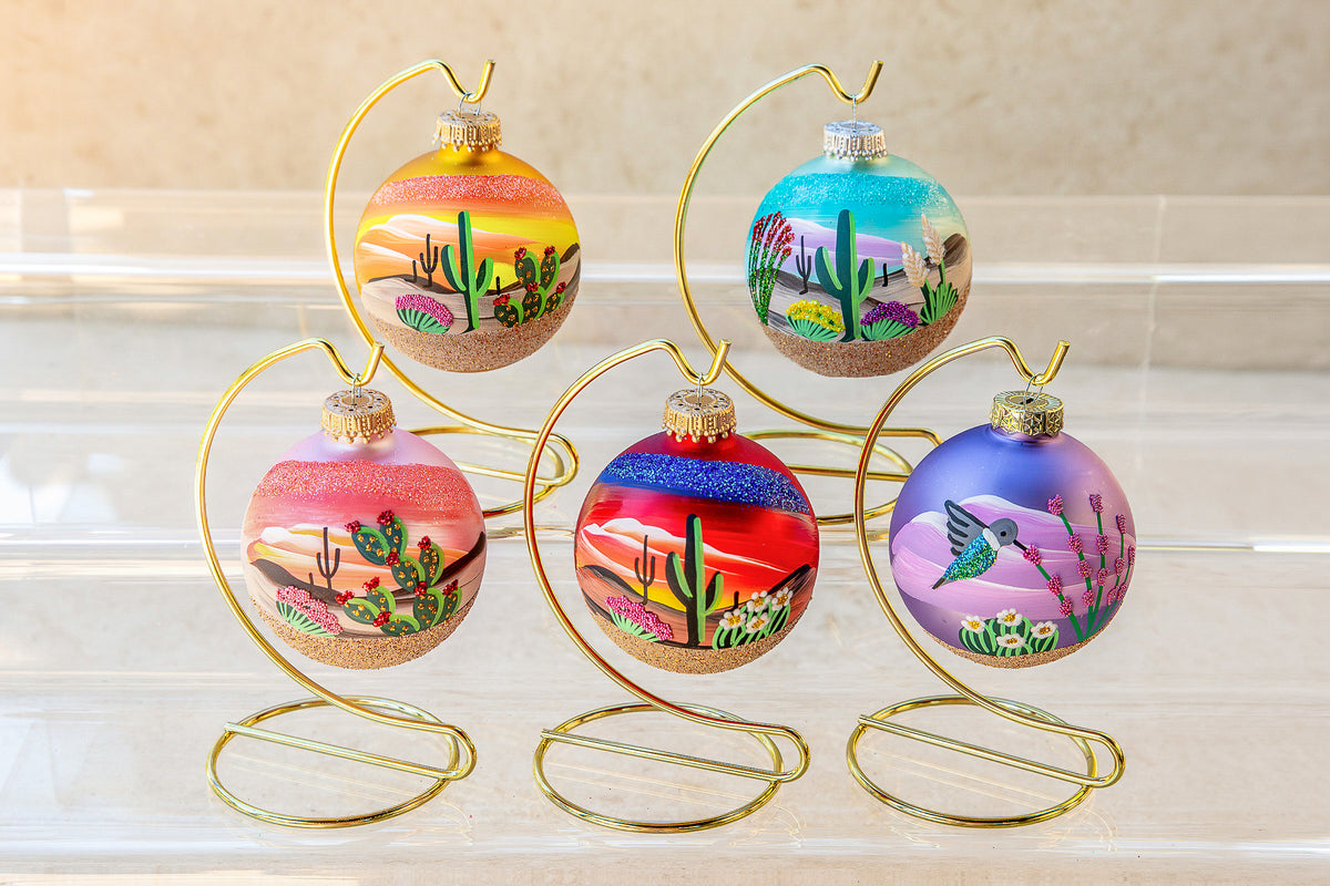 Five Hand Painted ornaments on gold stands: Arizona Sunrise, Desert in Bloom, Prickly Pear Cactus, Arizona Sunset, and a purple Hummingbird